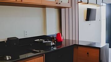 A modern kitchen with wooden cabinets, a black countertop, and a red kettle.