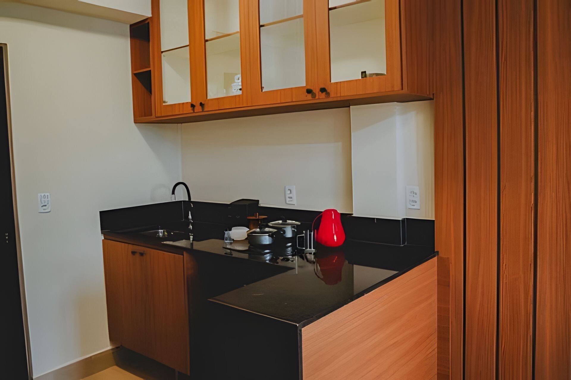 A compact kitchen with wooden cabinets, a black countertop, and a red kettle.
