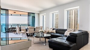 A modern living room with a black leather sofa, a glass coffee table, and a dining area with white chairs. - Absolute beachfront luxury in Surfers Paradise — a designer 3-bedroom apartment on level 11 of the iconic Peppers Soul tower. Panoramic ocean views, wraparound balcony, resort pools, spa & gym. Sleeps 6. Steps to the sand, 300m to Cavill Ave. (Surfers Paradise)