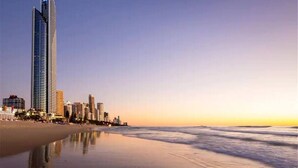 A beachfront hotel with a tall building, a sandy beach, and ocean waves. - Absolute beachfront luxury in Surfers Paradise — a designer 3-bedroom apartment on level 11 of the iconic Peppers Soul tower. Panoramic ocean views, wraparound balcony, resort pools, spa & gym. Sleeps 6. Steps to the sand, 300m to Cavill Ave. (Surfers Paradise)