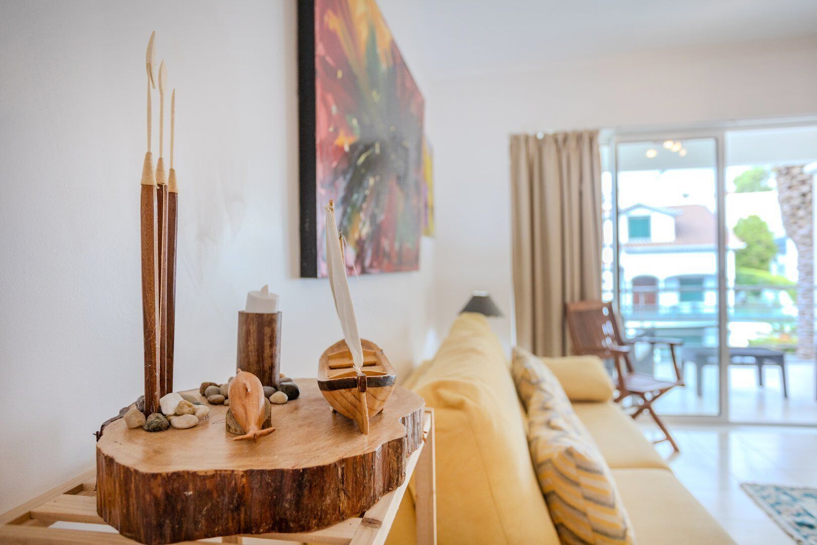 A wooden table with a rustic centerpiece, a yellow sofa, and a painting on the wall.