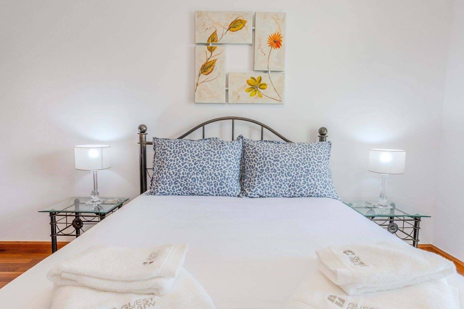 A neatly made bed with white linens, two leopard print pillows, and a wall art piece above it.