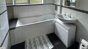 Un bagno moderno con vasca, lavandino e doccia. Una finestra permette l'ingresso di luce naturale e c'è uno specchio sopra il lavandino.