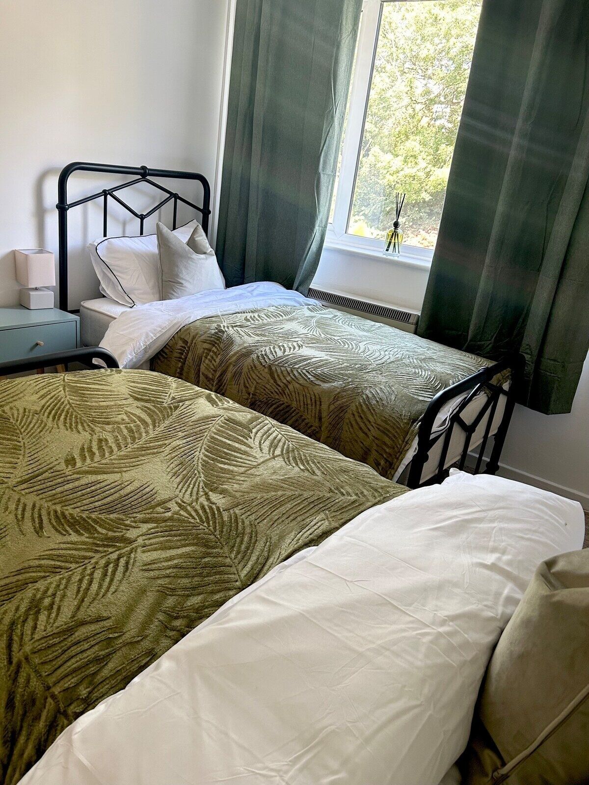 Quarto com duas camas, mesa de cabeceira, abajur e janela com cortinas.