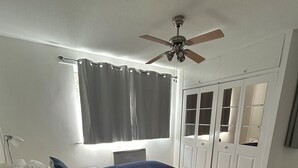Una camera da letto con un letto, un comodino, una ventola a soffitto, una finestra con tende e un armadio con ante a specchio.