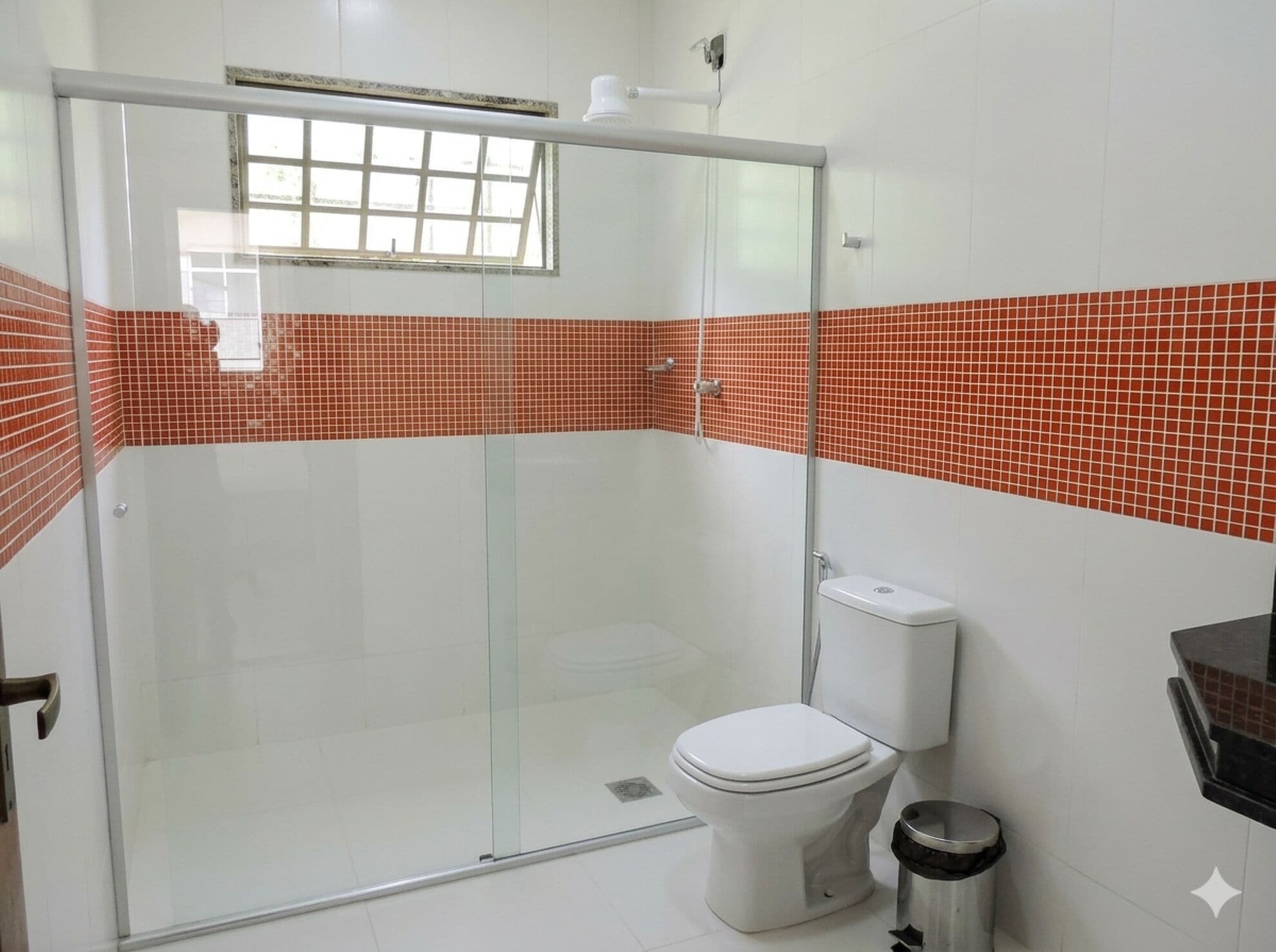 A bathroom with a glass shower enclosure, white toilet, and red-tiled walls.