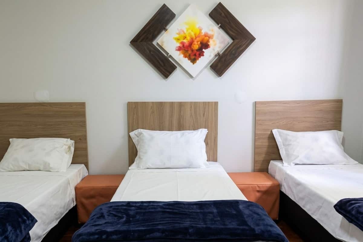 A hotel room with three beds, a wooden headboard, a wall-mounted artwork, and a wooden floor.