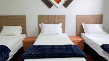 Quarto de hotel com três camas, cabeceira de madeira, uma obra de arte pendurada na parede e piso de madeira.