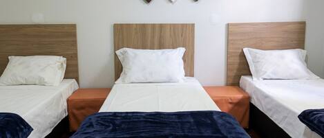 Habitación de hotel con tres camas, cabecera de madera, una obra de arte colgada en la pared y piso de madera.