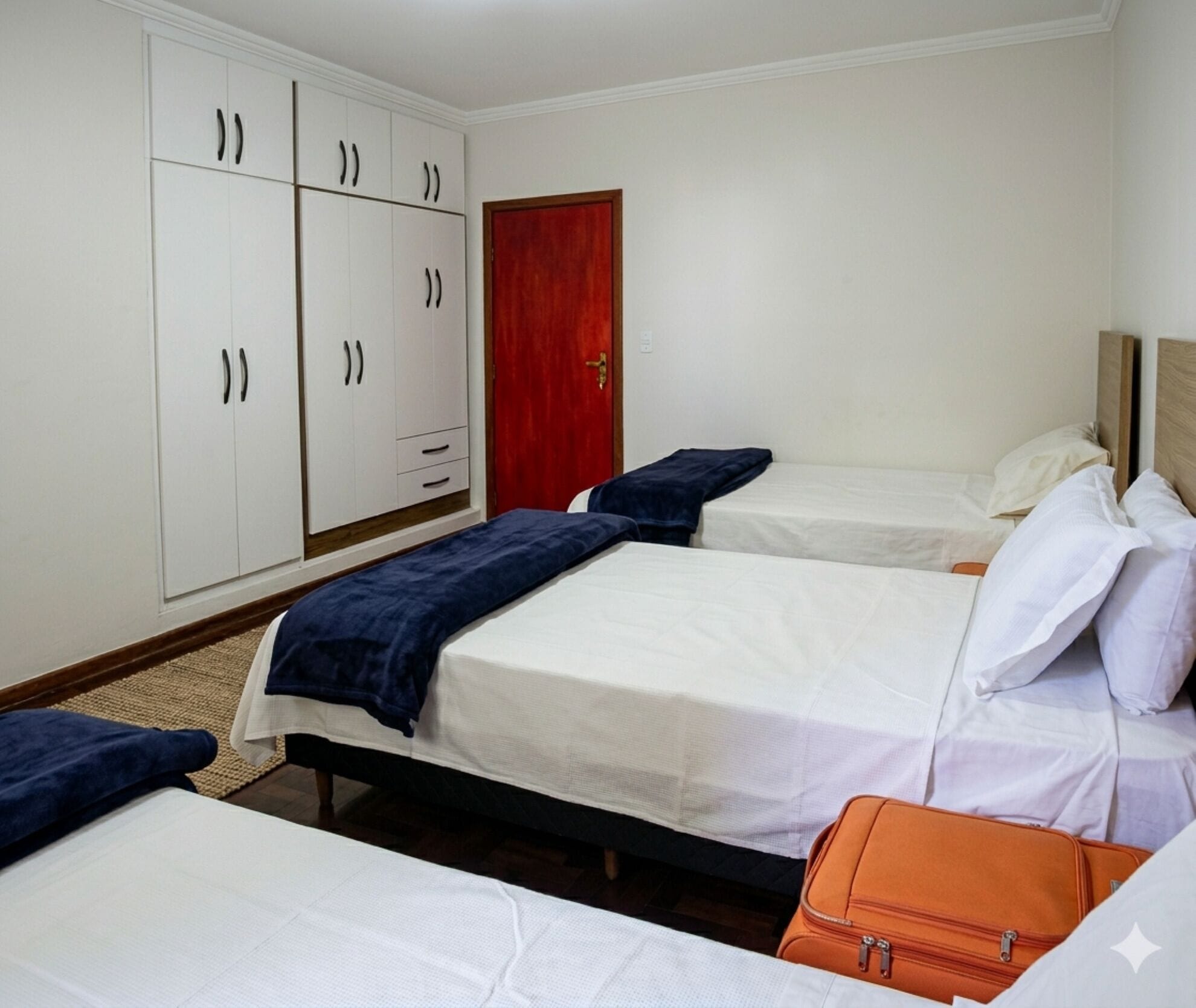 Habitació d'hotel amb dos llits, un armari i una porta vermella.