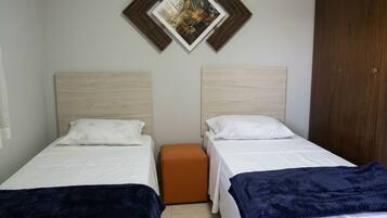 Quarto com duas camas de solteiro, um banquinho laranja pequeno e um guarda-roupa de madeira.