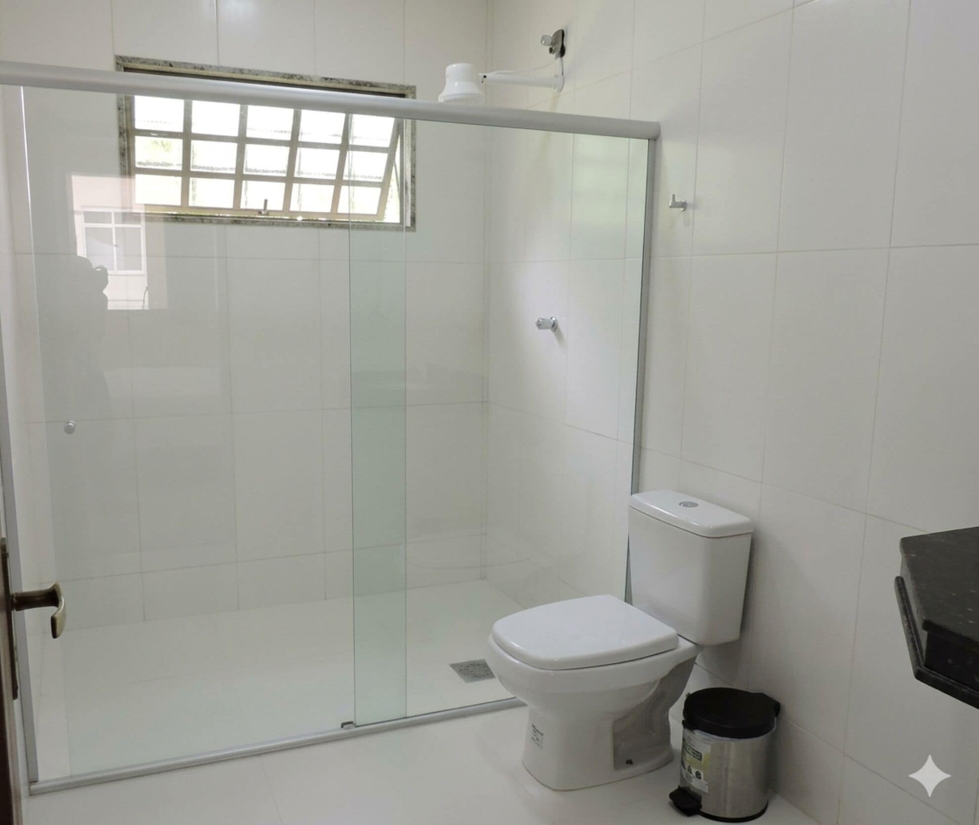 A bathroom with a glass-enclosed shower, a white toilet, and a trash bin.