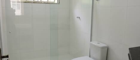 A bathroom with a glass-enclosed shower, a white toilet, and a trash bin.