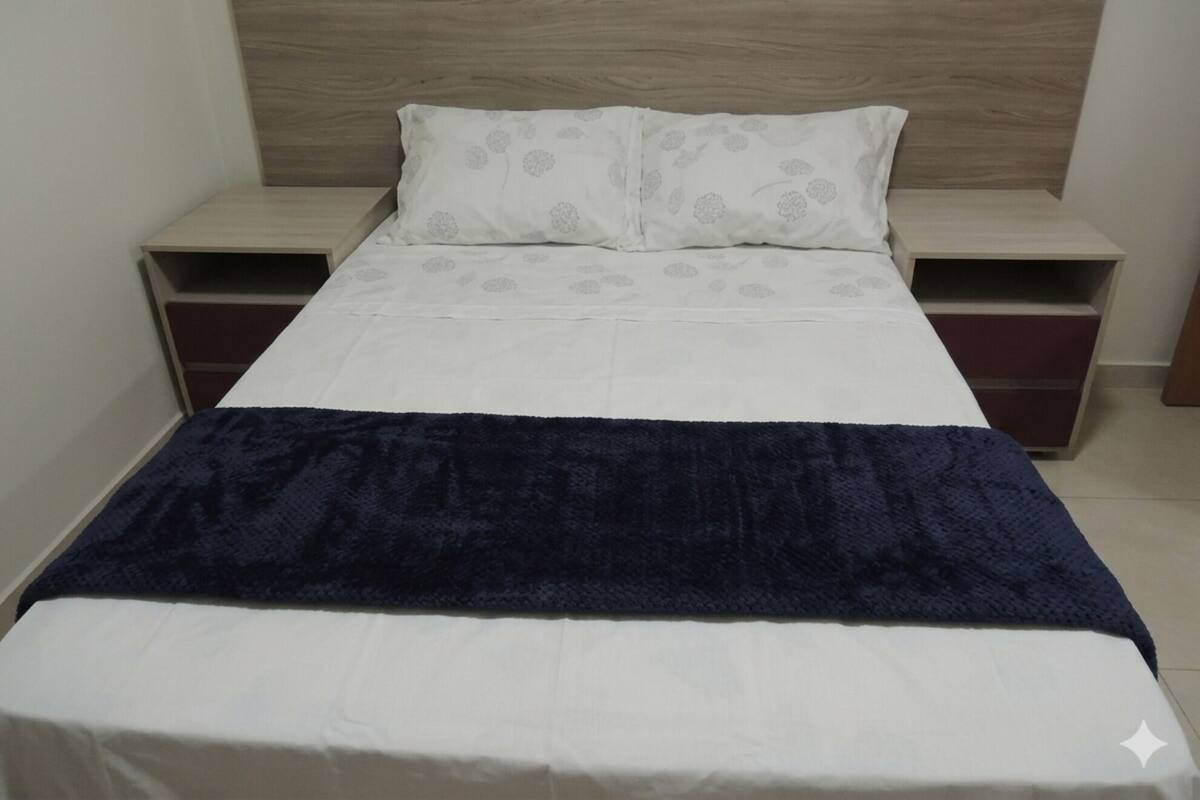 A single bed with a wooden headboard, a white pillow with a floral pattern, and a dark blue blanket. There are two bedside tables with drawers, one on each side of the bed.