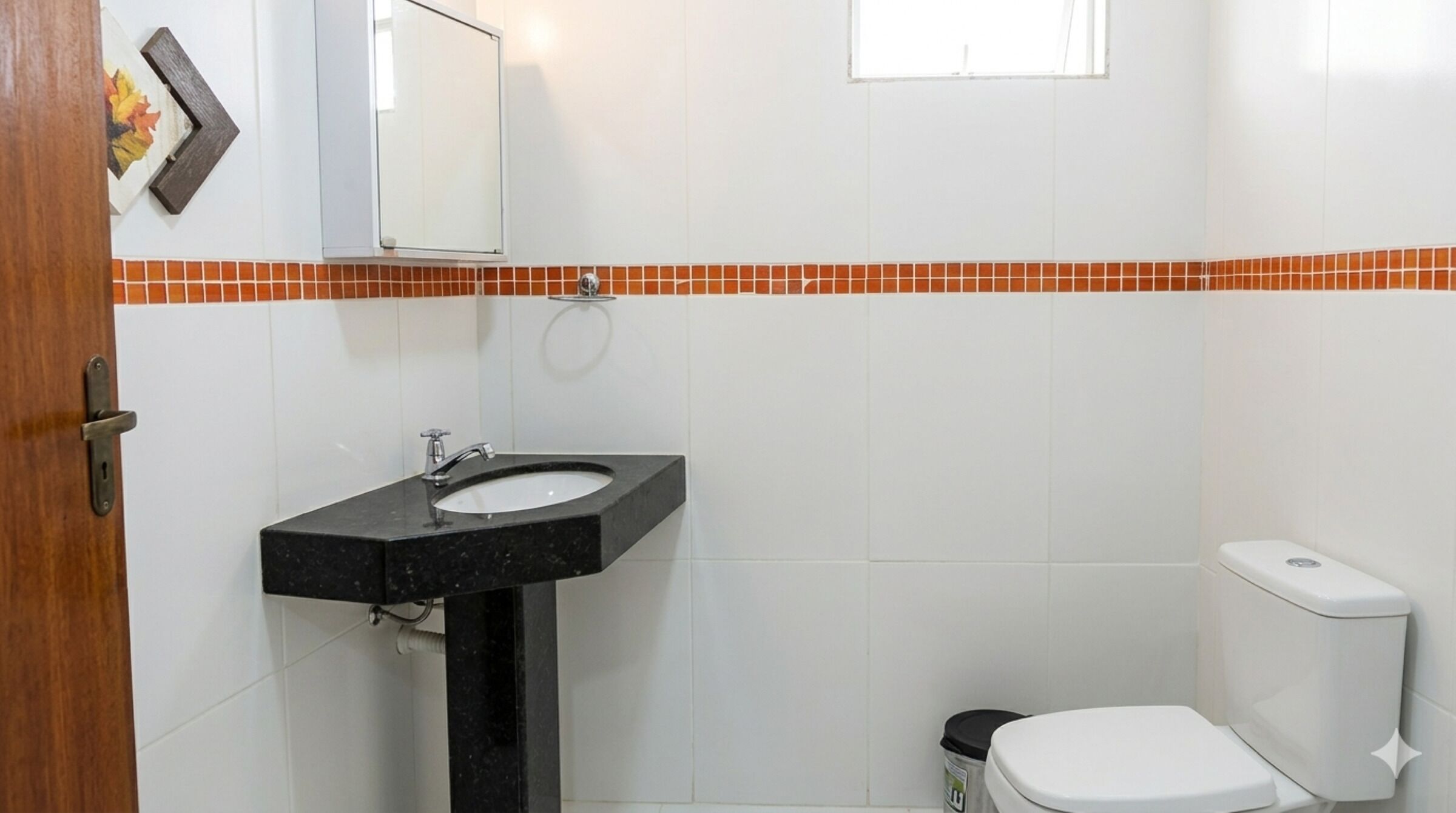 A bathroom with a black sink, white toilet, and orange-tiled backsplash.