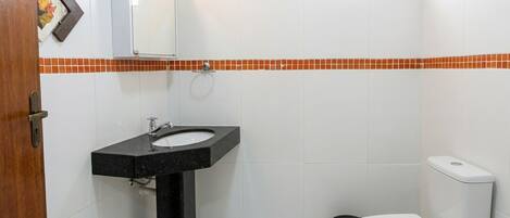 A bathroom with a black sink, white toilet, and orange-tiled backsplash.