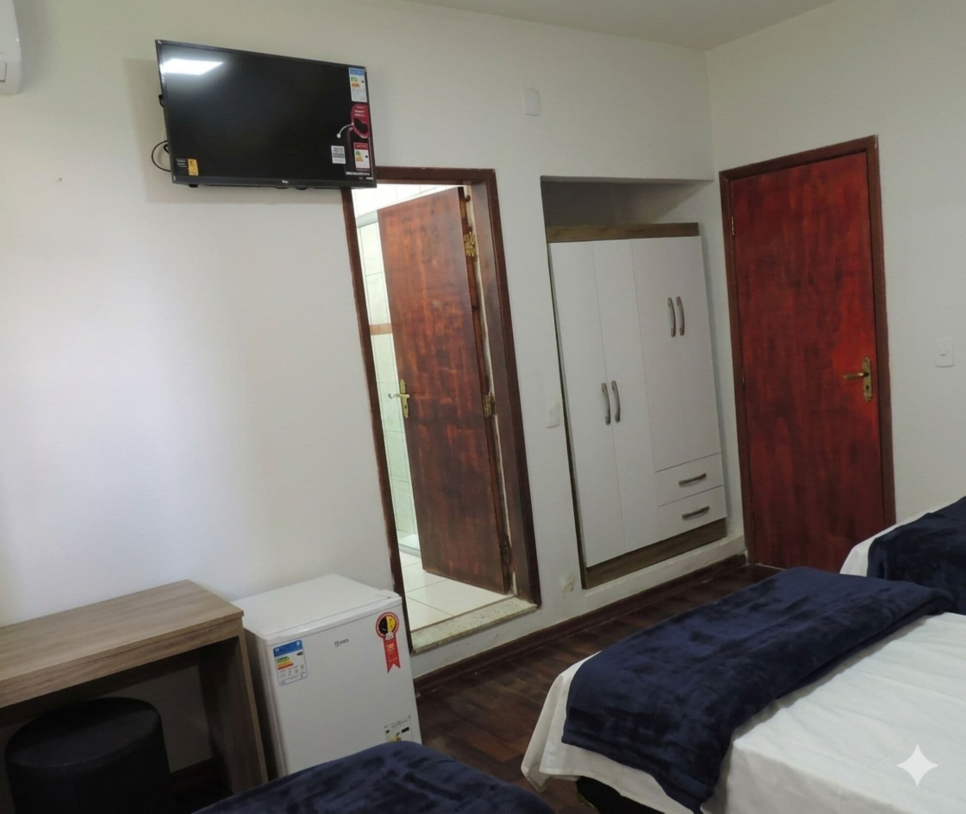 Een slaapkamer met een bed, een kledingkast, een spiegel, een televisie en een kleine koelkast.