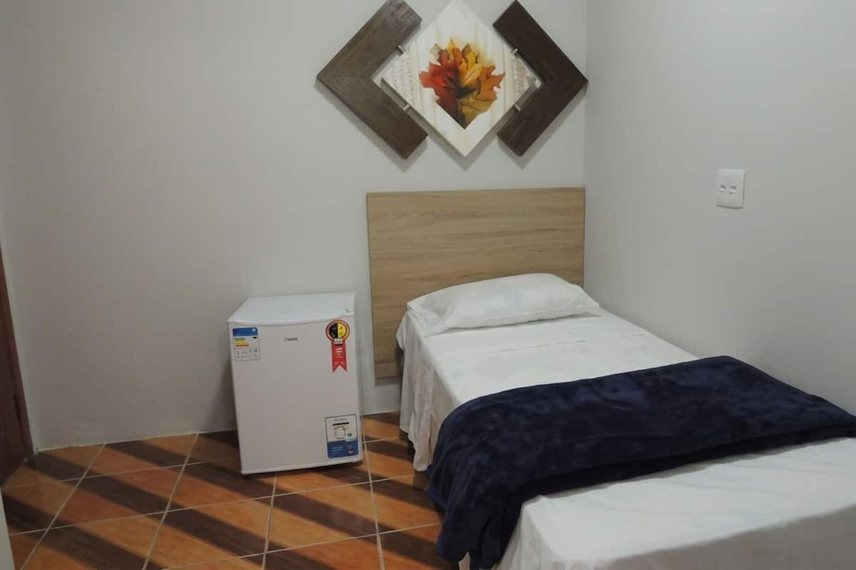 A small room with a bed, a refrigerator, and a wall-mounted decoration.