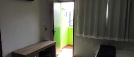 A room with a bed, a desk, a chair, a fan, and a window with curtains.