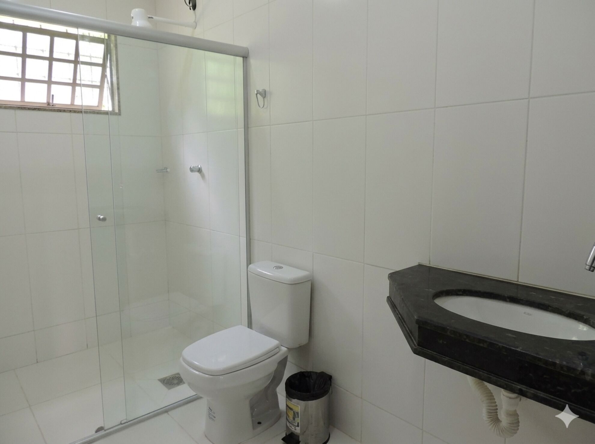 A bathroom with a glass shower enclosure, a white toilet, and a black sink with a white countertop.