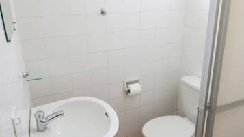 Casa de banho pequena com lavatório branco, sanita e porta de chuveiro em vidro.