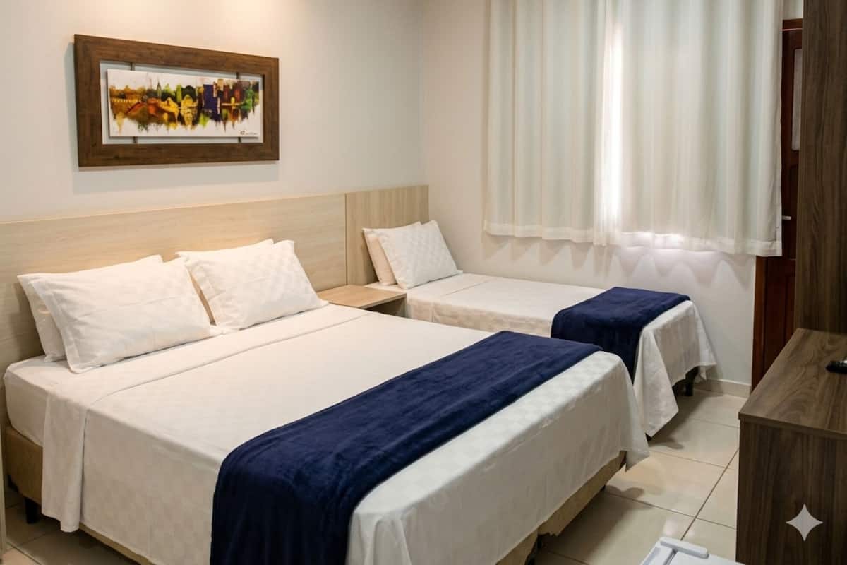 A hotel room with two beds, a wooden headboard, a framed picture on the wall, a window with curtains, and a wooden desk.
