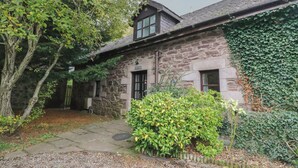 Un bâtiment en pierre doté d’un toit en pente, d’un petit porche et d’un jardin agrémenté de diverses plantes.