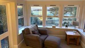 Une pièce chaleureuse avec une grande fenêtre, un fauteuil confortable, une petite table en bois et une lampe.