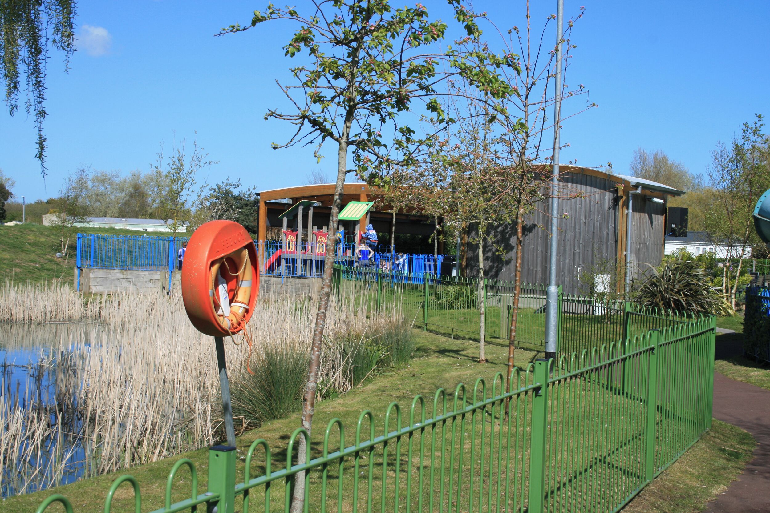 Uma área de parque cercada com um parquinho, um lago e um galpão.