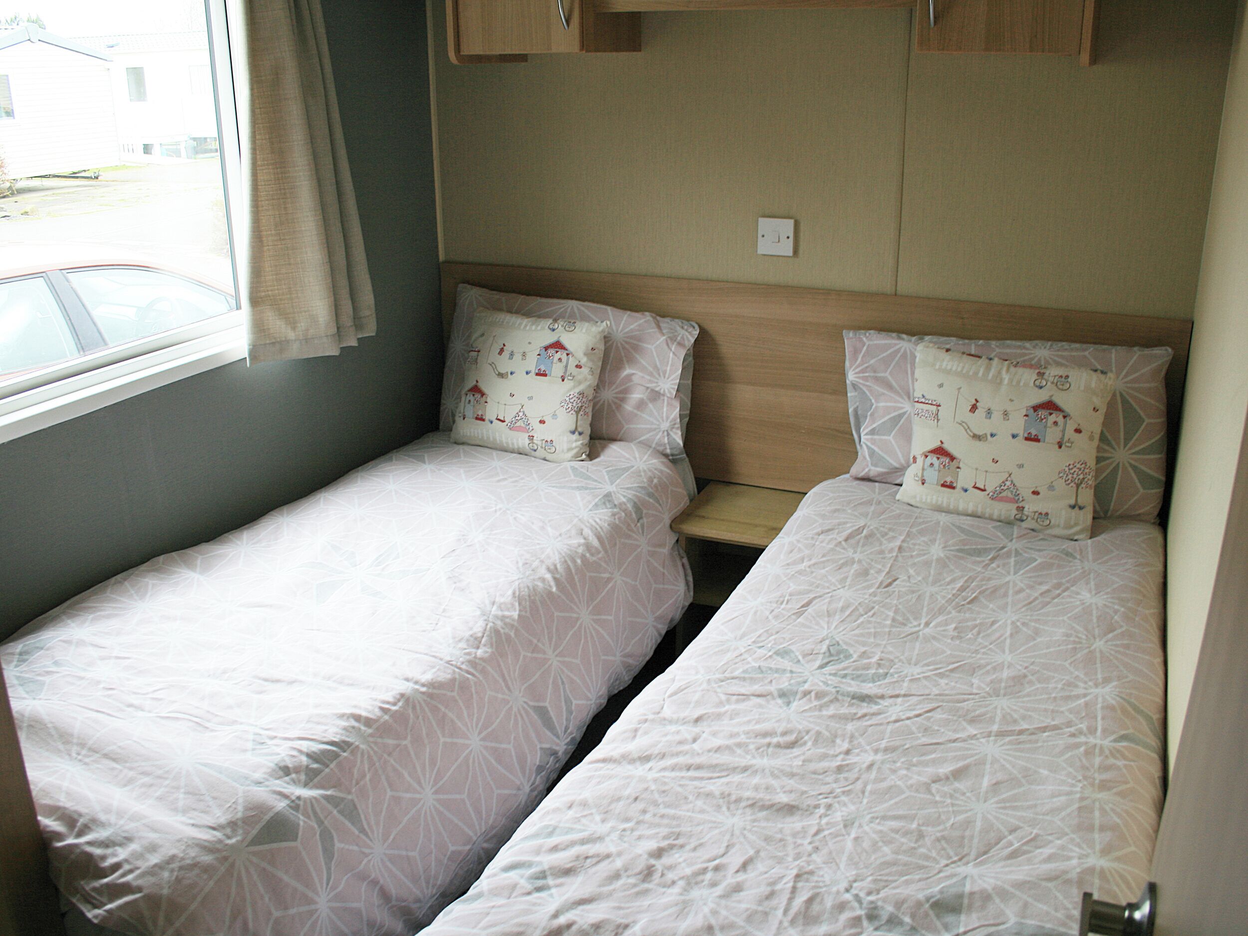 Een kleine, compacte kamer met twee éénpersoonsbedden, een raam en een deur.