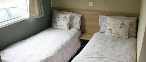 Een kleine, compacte kamer met twee éénpersoonsbedden, een raam en een deur.