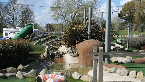 A water feature with a green slide, a small pond, and a wooden bridge.