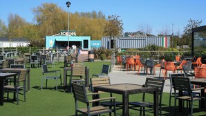 An outdoor seating area with tables and chairs, a blue container with a sign, and a pizza container.