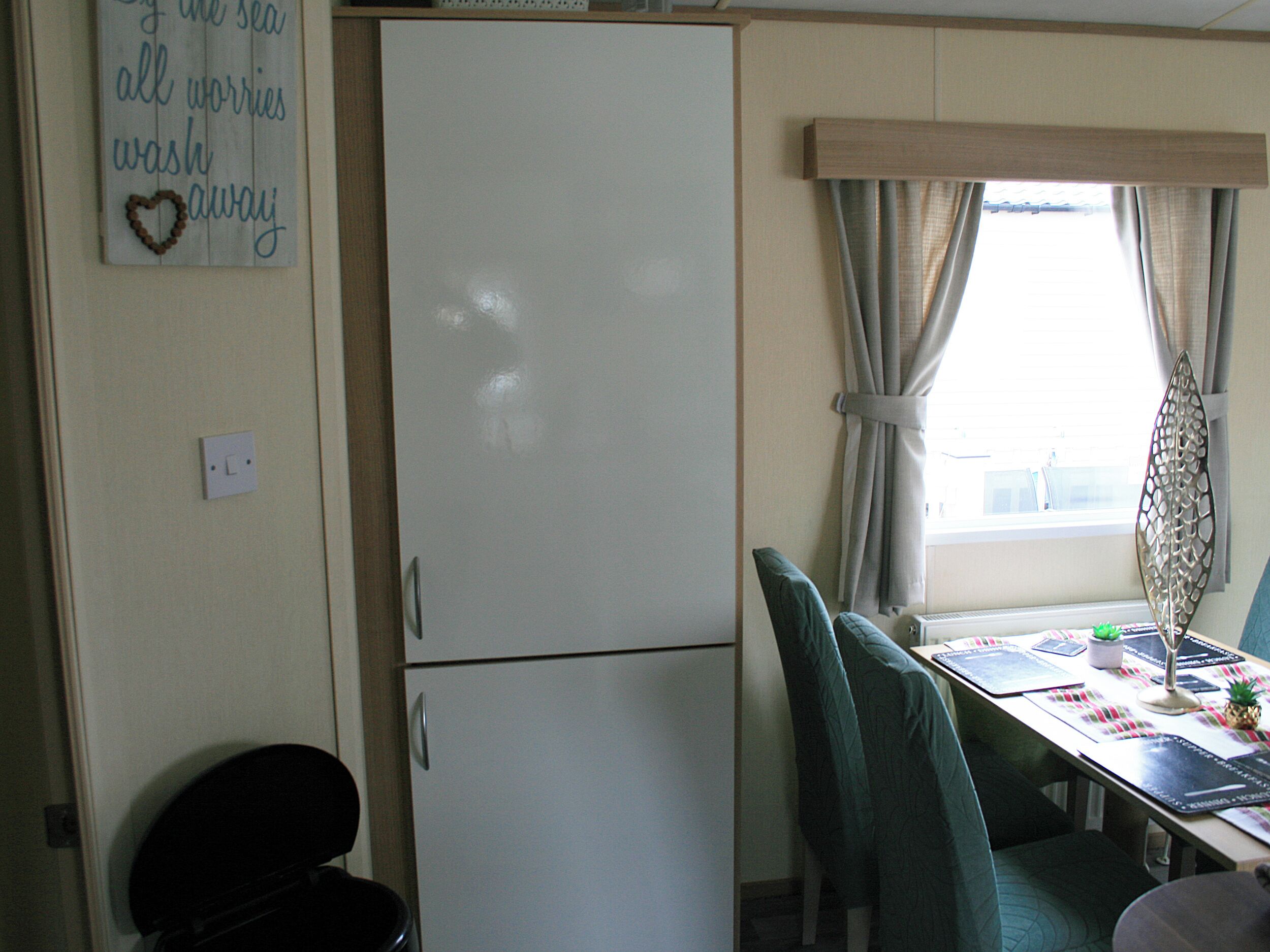 A compact room with a white refrigerator, a dining table with chairs, and a window with curtains.