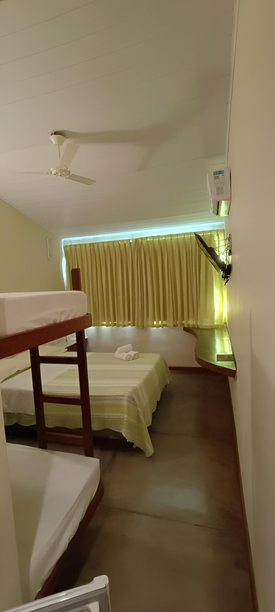 A room with two beds, a table, a ceiling fan, and a wall-mounted light fixture.