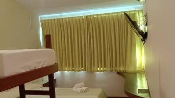 A room with two beds, a table, a ceiling fan, and a wall-mounted light fixture.