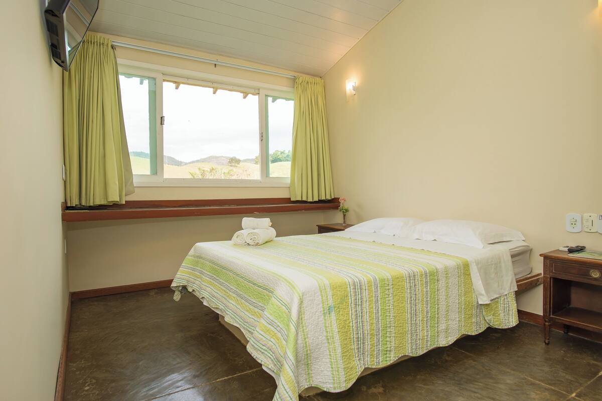 A bedroom with a bed, a window with curtains, a bedside table, and a nightstand.