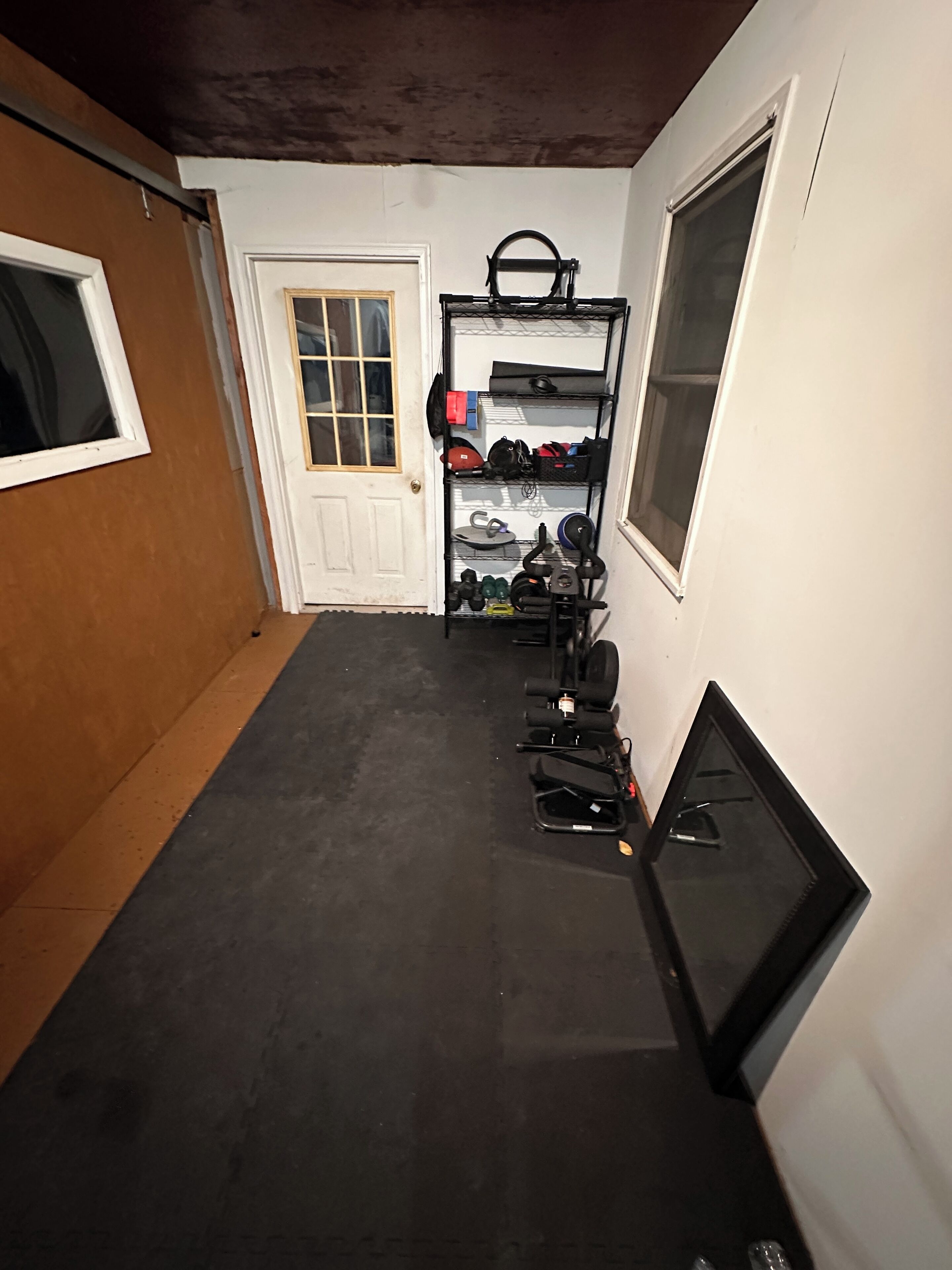 Une pièce de taille modeste, avec un plancher noir, une porte blanche et une fenêtre.