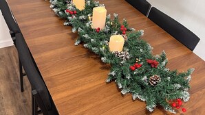 Ett långt matbord i trä, dekorerat med en girlang av vintergröna grenar, röda bär och kottar, samt ljus.