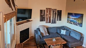 A living room with a fireplace, a television, a couch, and a painting of a landscape.