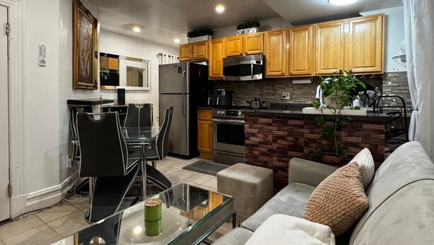 Una cocina moderna con armarios de madera, un refrigerador de acero inoxidable y un microondas. Hay una zona de comedor con una mesa de vidrio y sillas.
