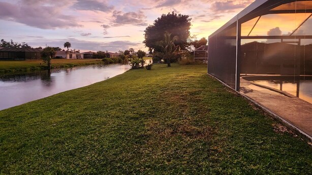 A modern building with a glass facade, a grassy area, and a body of water in the background. - Casa Mar Van Beautiful newly renovated Home on Canal Heated Pool w/Spa andLanai (Rotonda West)