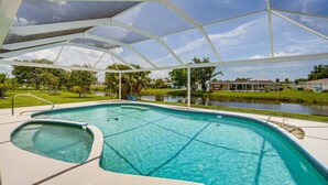 A swimming pool with a sunshade structure, surrounded by a grassy area and a body of water. - Casa Mar Van Beautiful newly renovated Home on Canal Heated Pool w/Spa andLanai (Rotonda West)