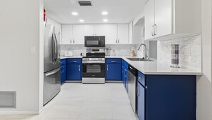 A modern kitchen with white cabinets, blue accents, stainless steel appliances, and a white countertop. - Casa Mar Van Beautiful newly renovated Home on Canal Heated Pool w/Spa andLanai (Rotonda West)