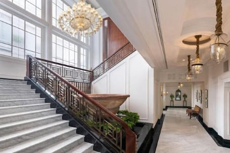 A grand staircase with a wooden railing, a chandelier, and a marble floor.. The Hermitage, a Tribute Portfolio Hotel, Jakarta