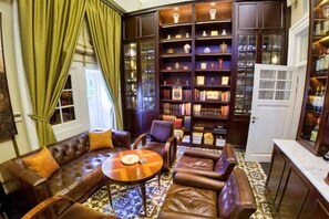 A room with a leather sofa, a round coffee table, and a bookshelf filled with books and decorative items. - The Hermitage, a Tribute Portfolio Hotel, Jakarta (Central Jakarta)