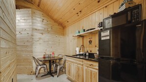 Une cuisine de taille réduite avec des murs en bois, un réfrigérateur noir et une table à manger avec des chaises.