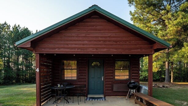 Une cabane en rondins avec une véranda, une table avec des chaises, un barbecue et un banc.