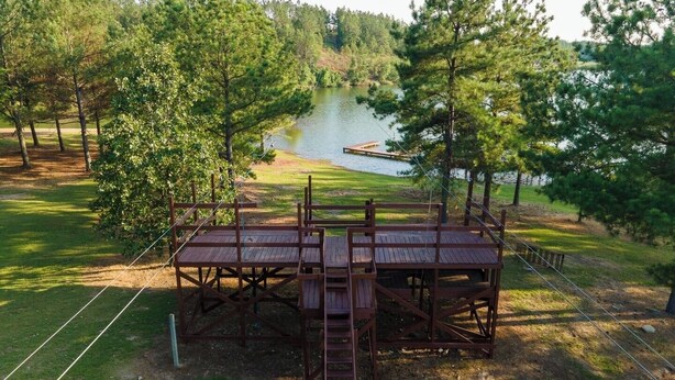 Une terrasse en bois avec une échelle menant à une plateforme d’où l’on a une vue sur un lac, le tout entouré d’arbres.