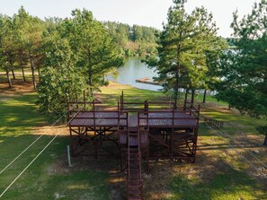 A wooden deck with a ladder leading to a platform overlooking a lake, surrounded by trees. - Timber Lodge Ranch - Studio 1 (Amity)